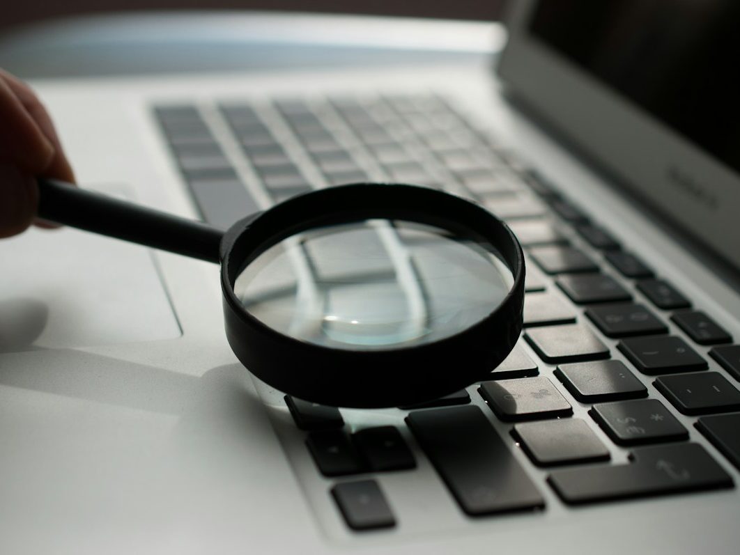 Documentación del AI Act evidencias y revisión Lupa sobre un portátil, representando la revisión de la documentación y las evidencias que exige el AI Act a una empresa