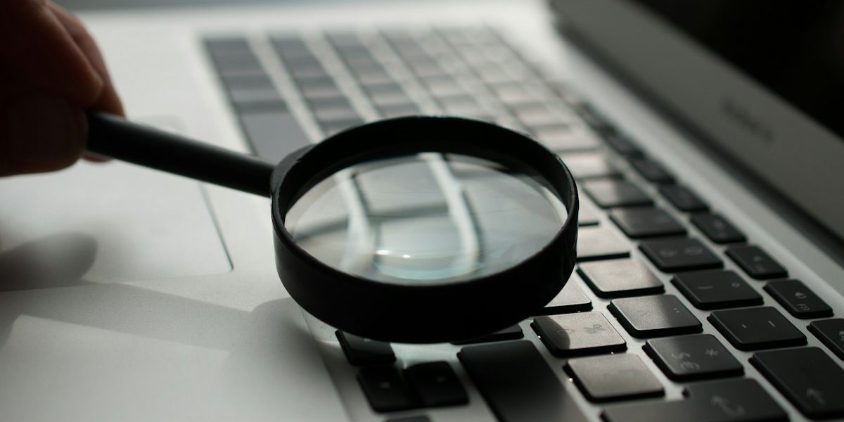 Lupa sobre un portátil, representando la revisión de la documentación y las evidencias que exige el AI Act a una empresa