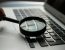Lupa sobre un portátil, representando la revisión de la documentación y las evidencias que exige el AI Act a una empresa