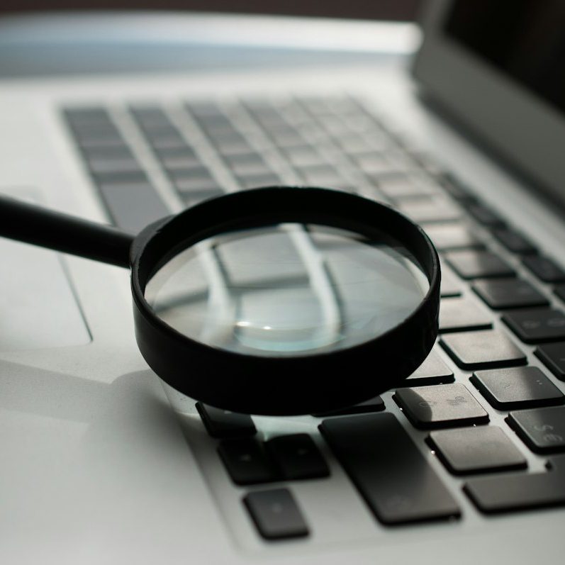 Lupa sobre un portátil, representando la revisión de la documentación y las evidencias que exige el AI Act a una empresa