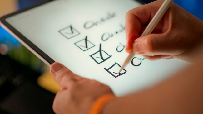 Inventario de sistemas de IA AI Act lista de verificación Mano marcando elementos en una lista de verificación, representando el inventario de sistemas de inteligencia artificial de una empresa